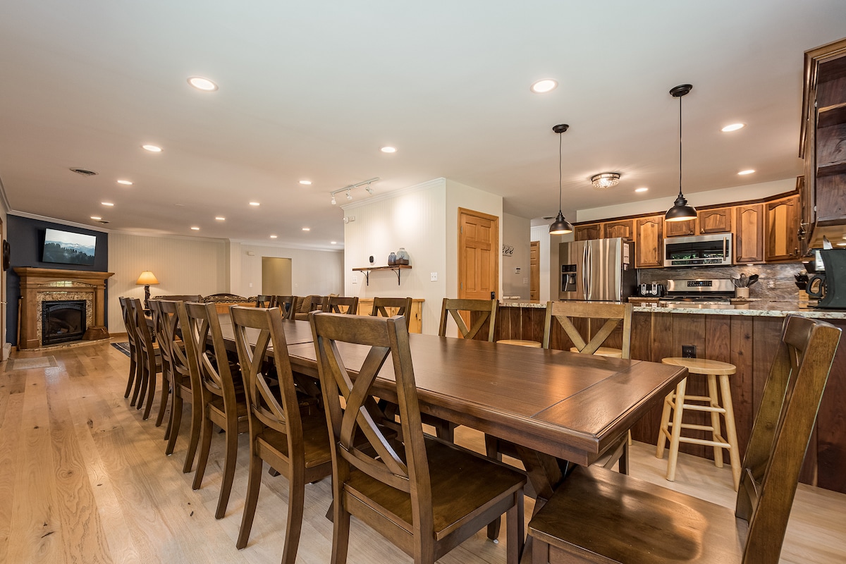 Long wooden dining table beside an open kitchen for communal meals